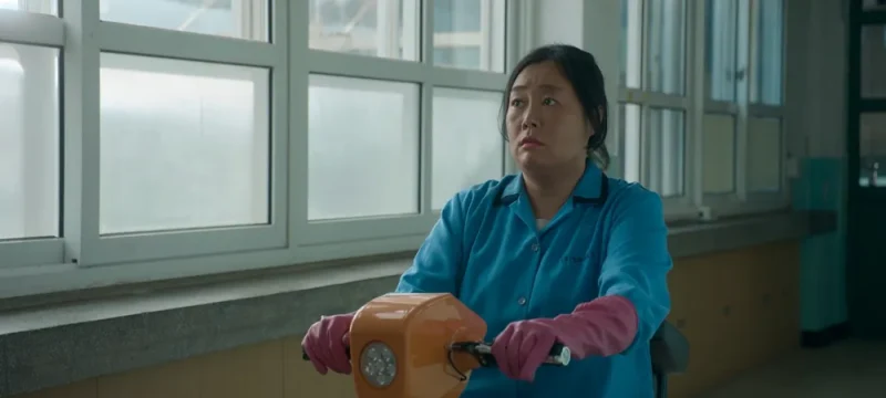 교실 복도에서 파랑 작업복과 고무 장갑을 끼고 청소하는 드라마 무빙의 미화원 캐릭터