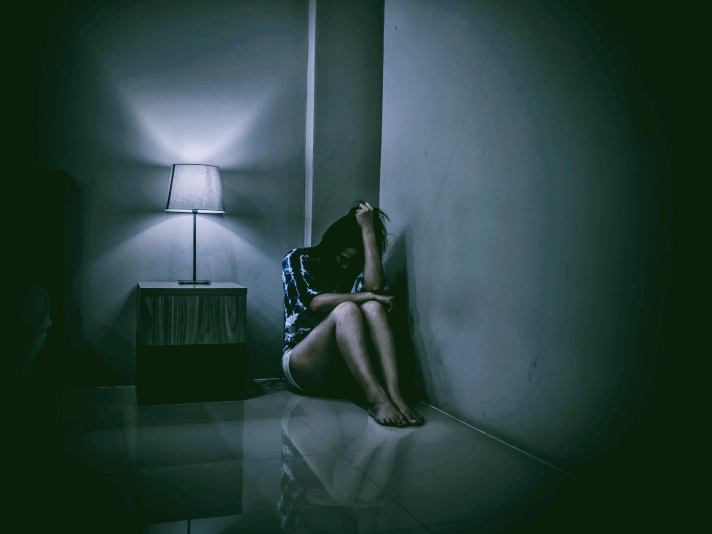 공황장애 증상 자가진단 치료 극복법에 관한 글의 이해를 돕기위한 이미지 : 여성이 방의 한 구석에 쪼그리고 앉아 괴로워하는 모습