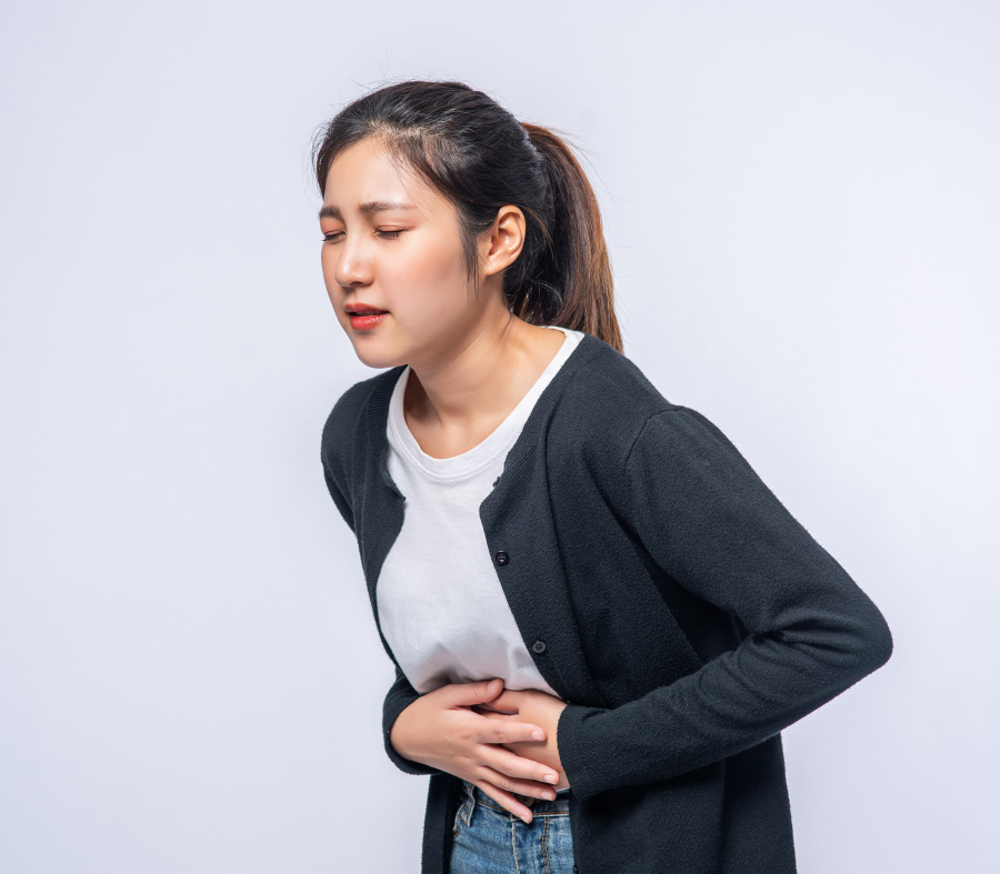 한 젊은 동양 여성이 소화불량으로 인해서 복통이 발생하여 양쪽 손으로 명치를 누르며 고통을 참고 있는 것을 찍은 사진