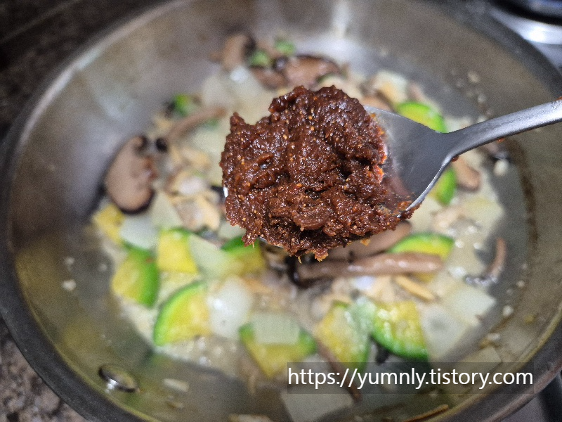 Holding a spoonful of Korean soybean paste (doenjang) over a frying pan