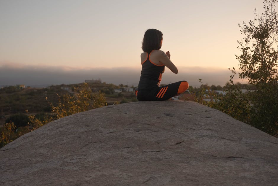 A woman in activewear meditating on a rock at sunset, embracing tranquility.