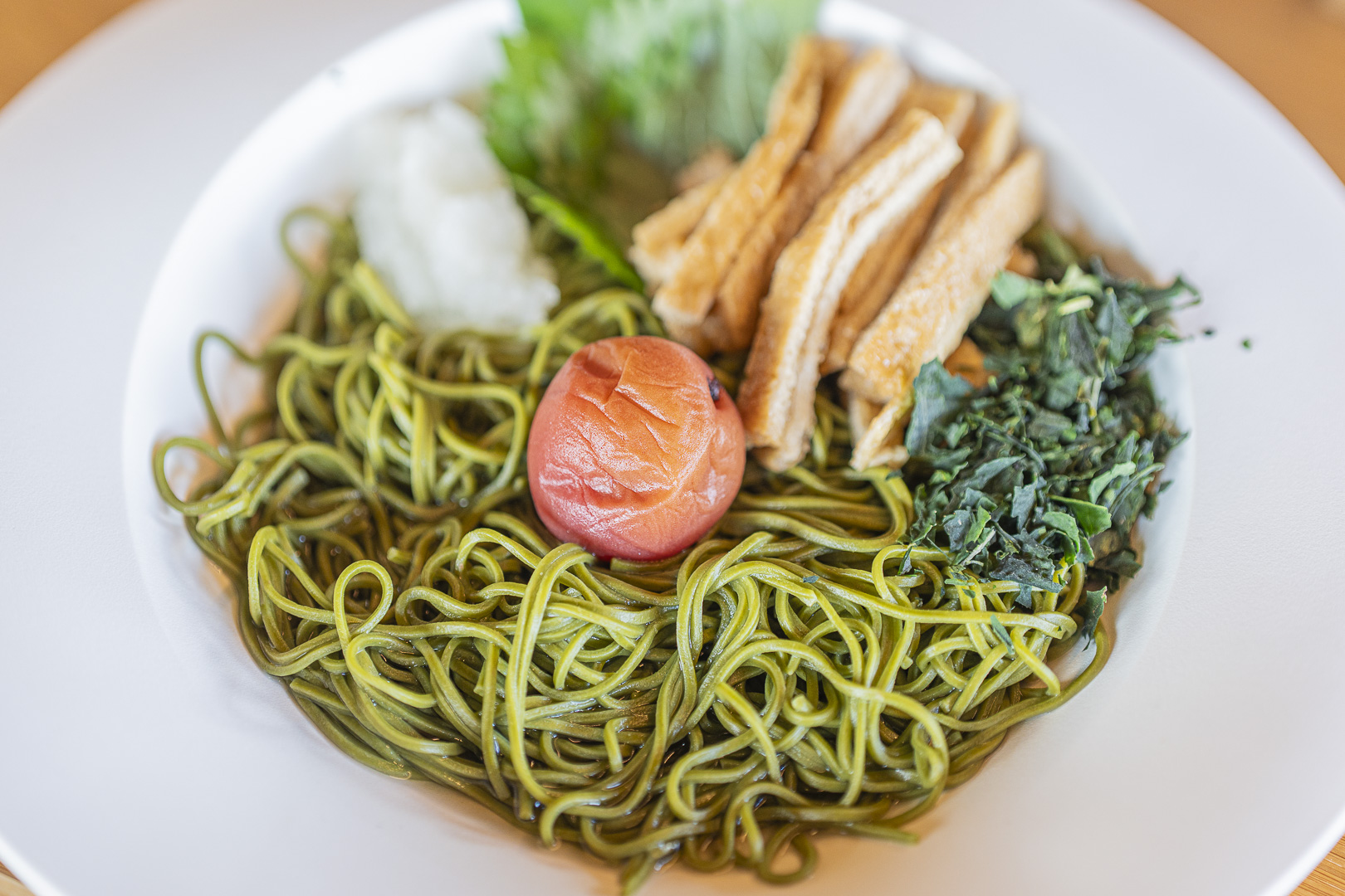 Nakamura Tokichi Byodoin: green noodles topped with plum, fried-tofu pieces, leafy greens and grated daikon in a white bowl.