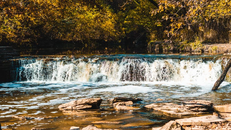 A serene waterfall flows gently surrounded by autumn foliage and rocks.