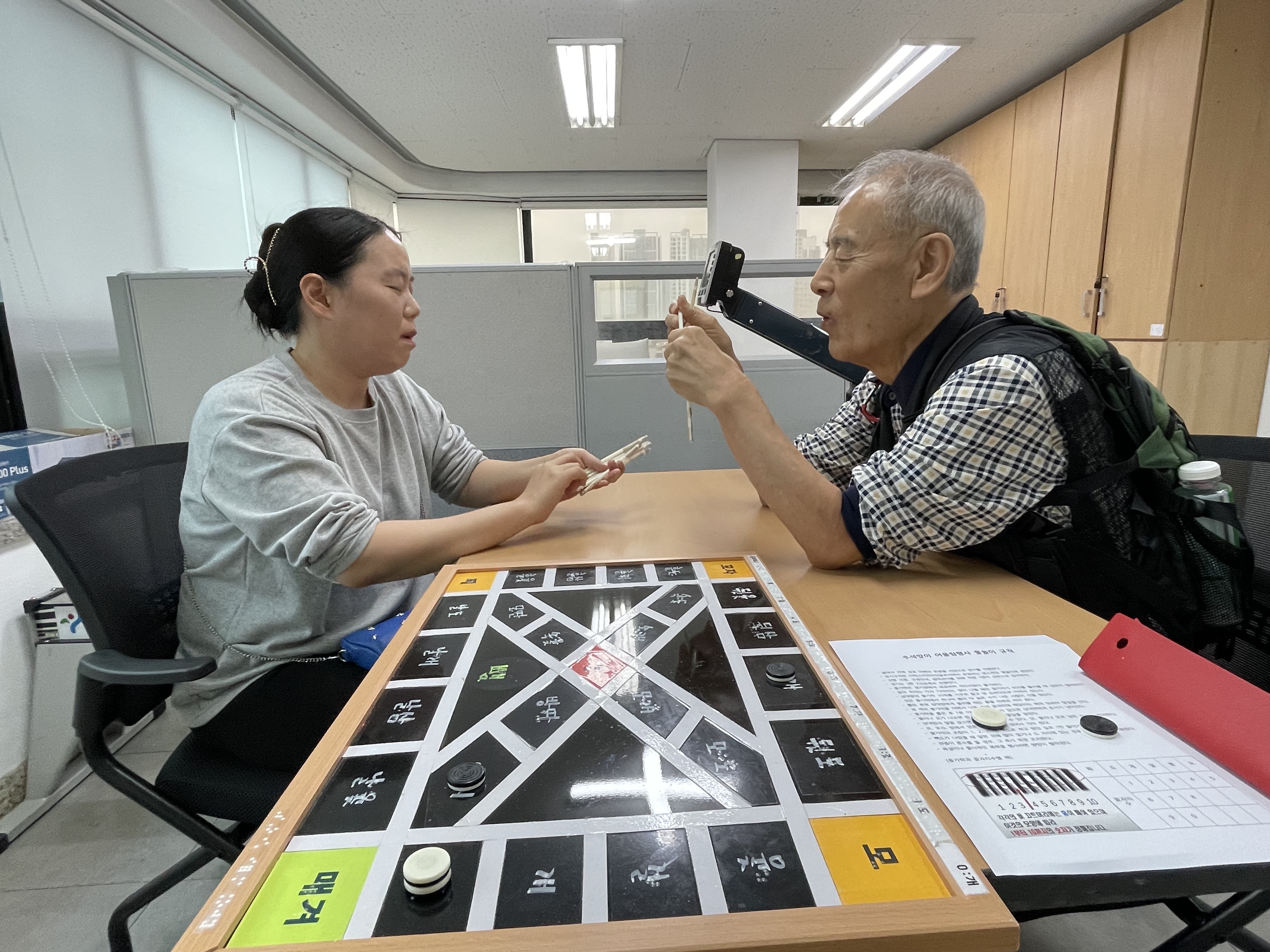 이미지 설명: 1부 윷놀이 경기사진. 이근호 지회원과 최정금 지회원이 경기중임.