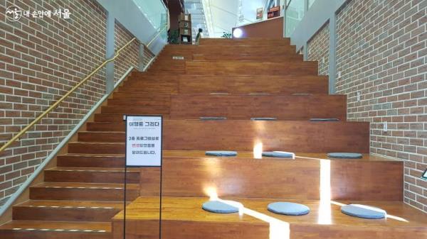 2층으로 올라가는 계단 옆, 긴 목재 의자와 방석이 편안한 느낌을 준다.