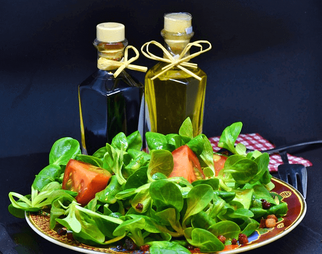 접시에 샐러드가 가득하고 뒤에는 식초병과 올리브유병이 2개 있다.