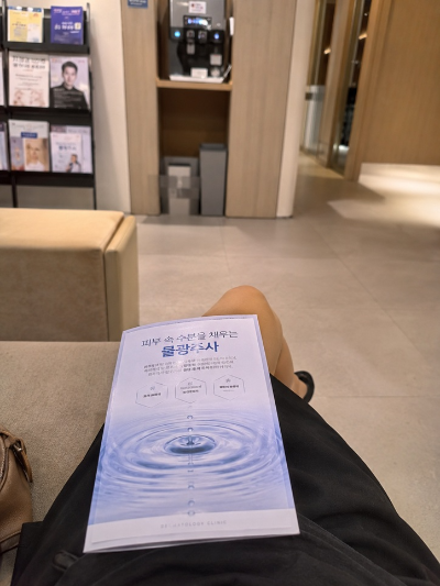 피부과 대기실 소파에 앉아 무릎 위에 물광주사 시술 안내 책자를 올려두고 대기 중인 내돈내산 현실적인 모습