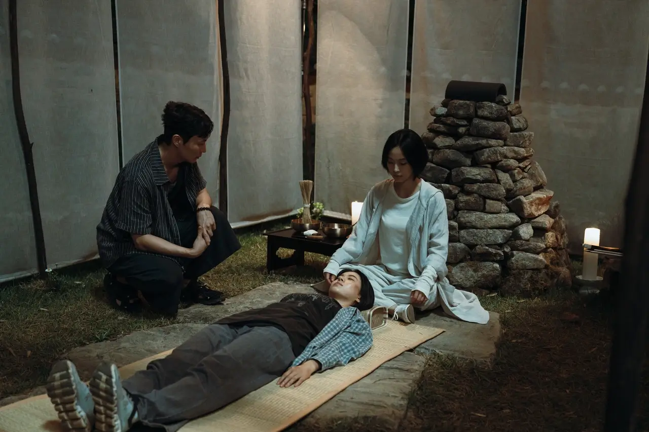 넷플릭스 기리고 스틸컷 속 누워있는 사람을 바라보는 여자와 남자