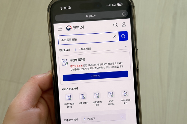 정부24 모바일 화면에서 주민등록등본을 검색하고 신청하는 모습의 자연스러운 스마트폰 사진