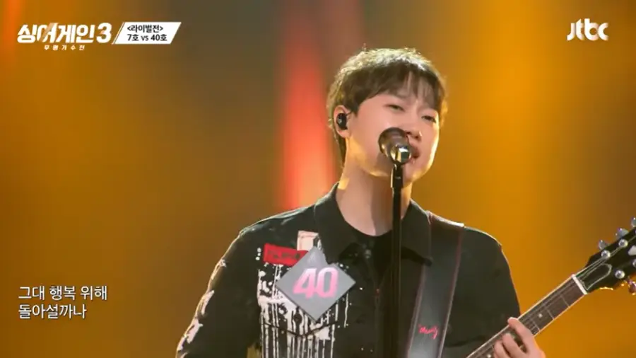 싱어게인3-
황금색 배경 검정색 셔츠에 기타를 들고 스탠딩마이크에 대고 노래하는 모습