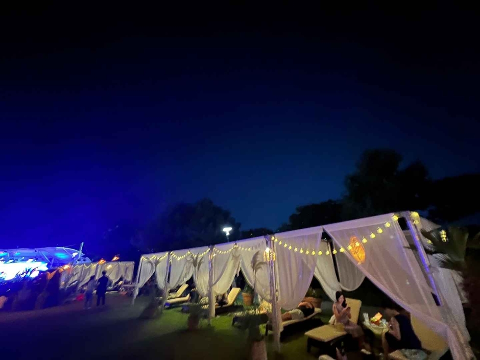 맑은 밤하늘 아래 대전 맥주축제장에 준비된 흰색 천으로 이루어진 천막에 노란색 전등이 달려있고 천막 안에는 누울 수 있는 베드가 준비되어있음.