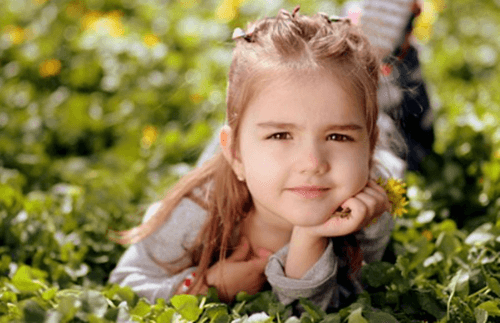 풀밭에 귀여운 소녀가 턱 받침을 하고 있는 사진