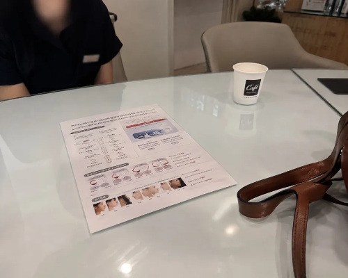 피부과 상담실 테이블 위에 놓인 기미 레이저 시술 안내 리플렛과 종이컵 사진