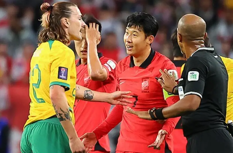 호주전- 노란상의 초록바지 호주선수가 검은색 상하의를 입은 심판에게 항의하고 이가운데서 말하고 있는 붉은유니폼 손흥민