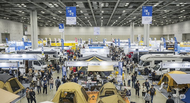 벡스코 박람회장 내부의 활기찬 모습. 다양한 캠핑 부스들이 전시되어 있고, 방문객들이 구경하고 있다.