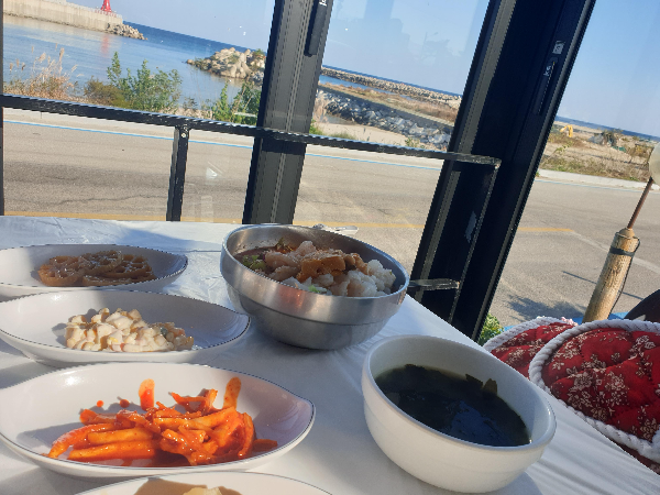 창 너머로 바다가 보인다. 테이블 위에는 주문한 음식들이 놓여 있다.