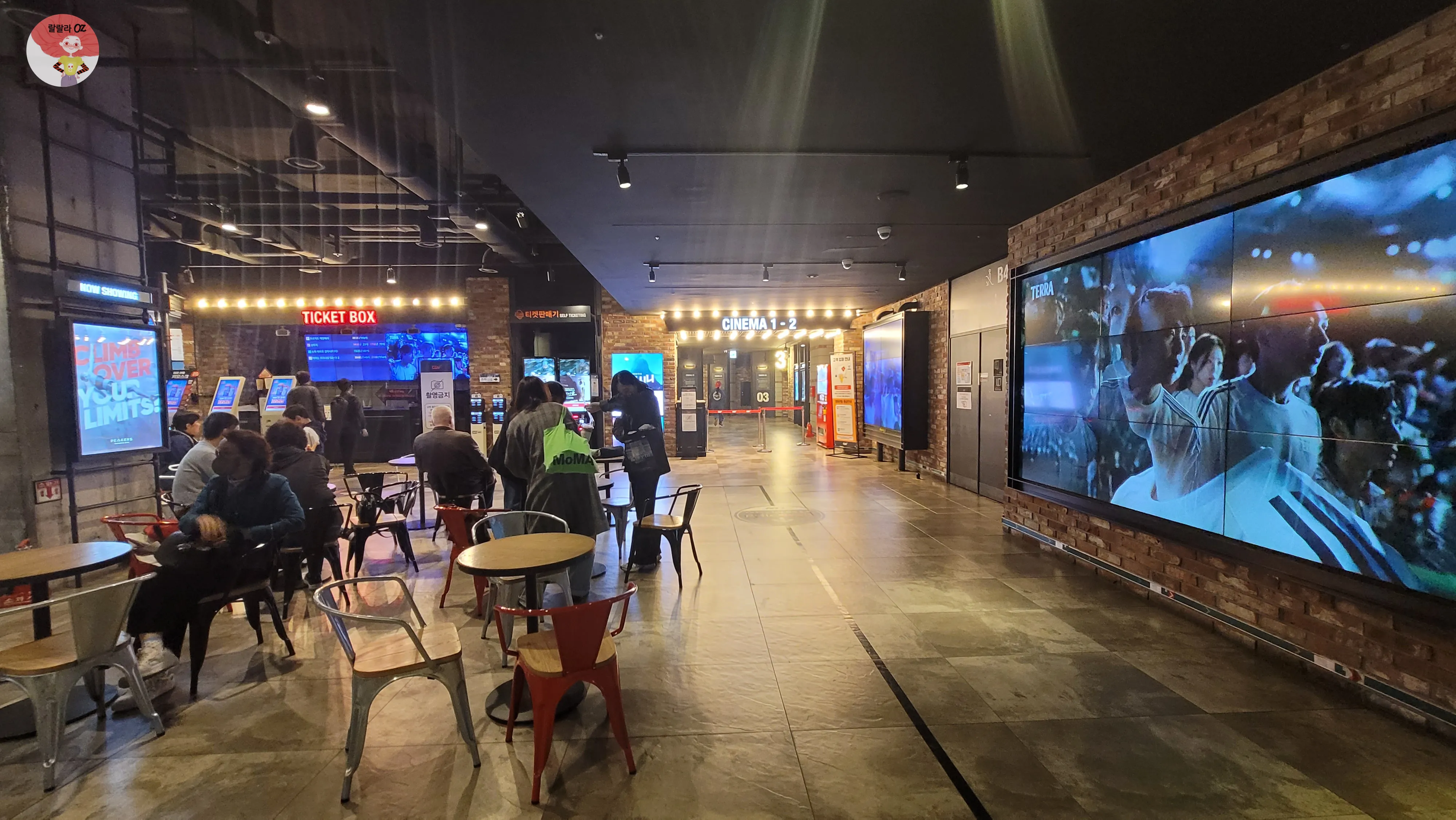 서울 종로구 CGV 피카디리1958 극장 내부 로비. 중앙에는 티켓박스와 무인 발권기가 있고&amp;#44; 오른쪽에는 &lsquo;CINEMA 1&middot;2&rsquo; 입구가 보인다. 관객들이 테이블에 앉아 있거나 티켓을 구매하며 대기 중.