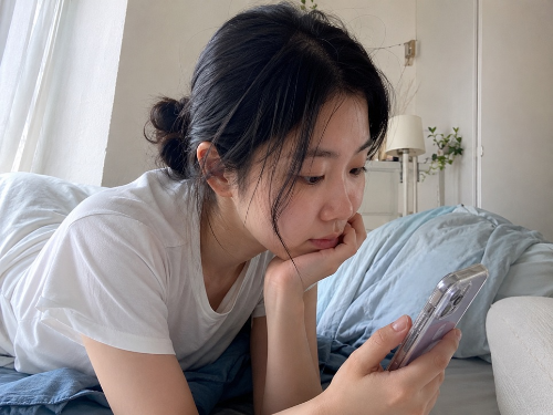 침대에서 스마트폰을 보며 고개를 숙인 20대 여성의 모습