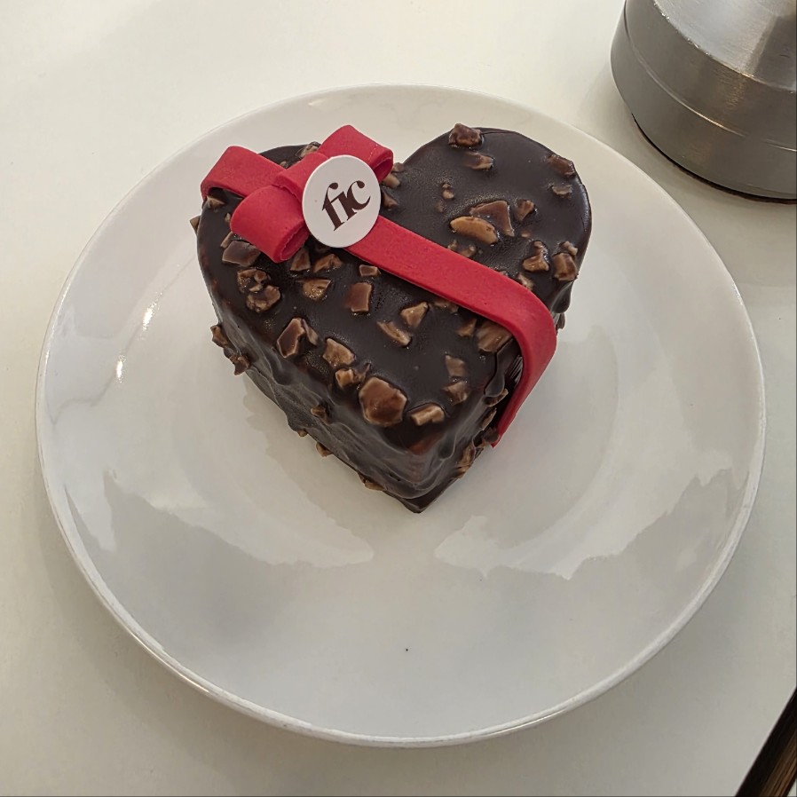 하트 모양 초콜릿 케이크 단품 클로즈업, 견과류 토핑과 레드 리본 장식
