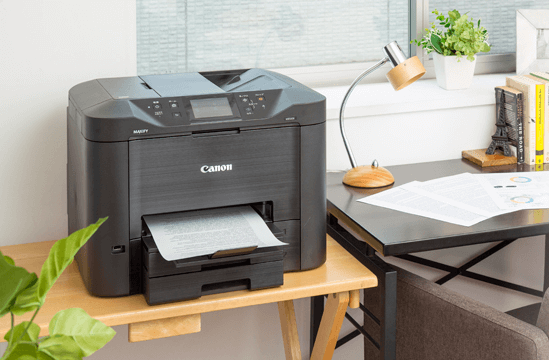 책상 위에 놓인 캐논 프린터가 문서를 출력 중인 사무실 공간