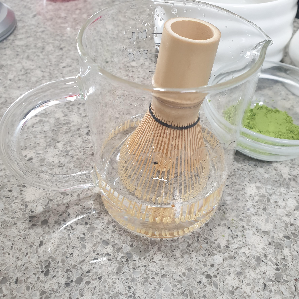 비이커에 물과 차선이 담겨있다. 옆에 말차 가루도 보인다.