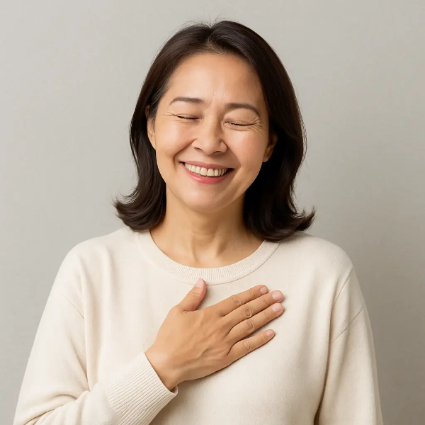 눈을 감고 미소 지으며 가슴에 손을 얹고 있는 여성의 안정된 표정이 담긴 텍스트 없는 인물 이미지