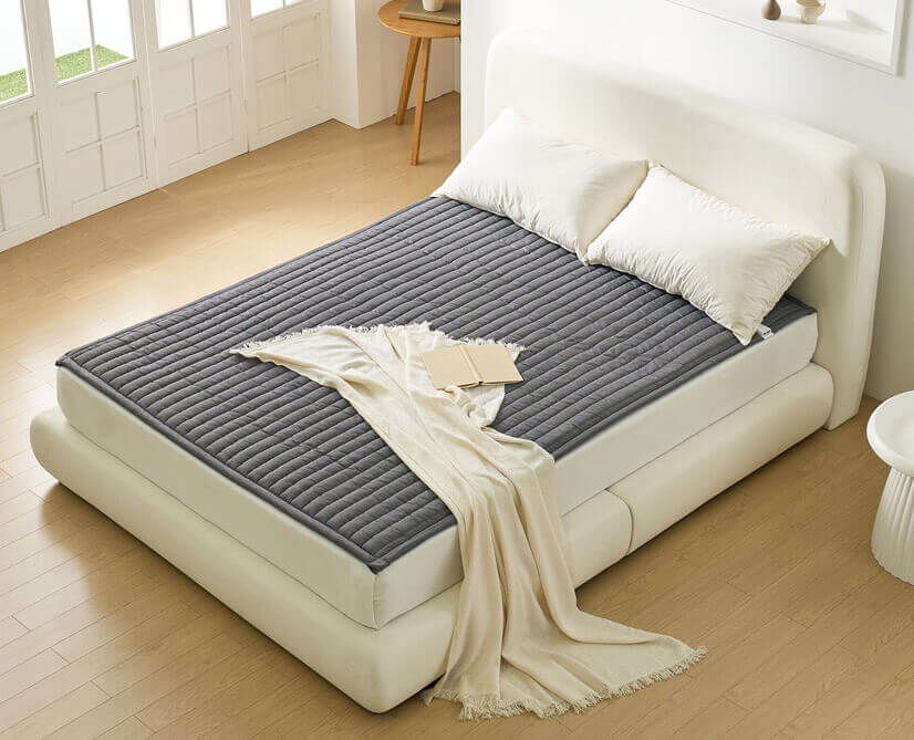 방안 하얀 침대 위에 놓인 회색 전기매트