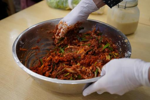위생장갑을 낀 손으로 커다란 스테인리스 볼 안에서 김치 양념과 채소를 버무리는 모습