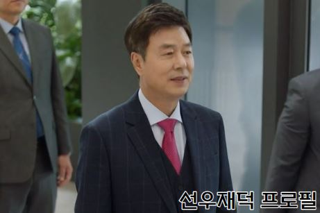 선우재덕이 양복을 입고 있으며 빨간 넥타이를 하고 있음