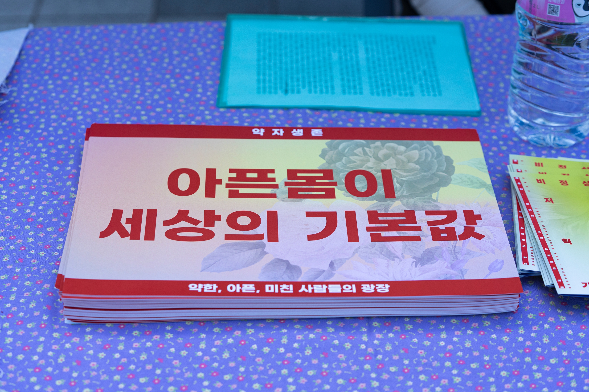 <약자생존> 행진 피켓이 테이블에 놓여 있다. 사진은 '아픈몸이 세상의 기본값'.