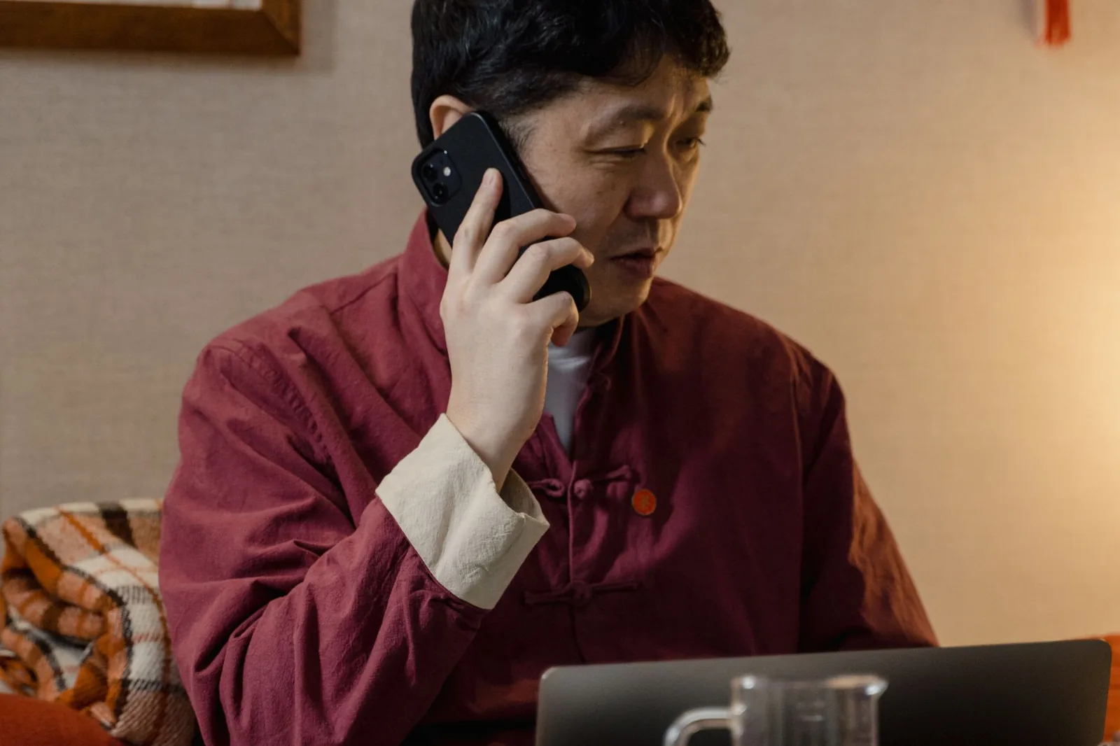 전통 의상을 입은 성인 남성이 실내에서 노트북으로 작업하면서 전화 통화를 하고 있습니다.