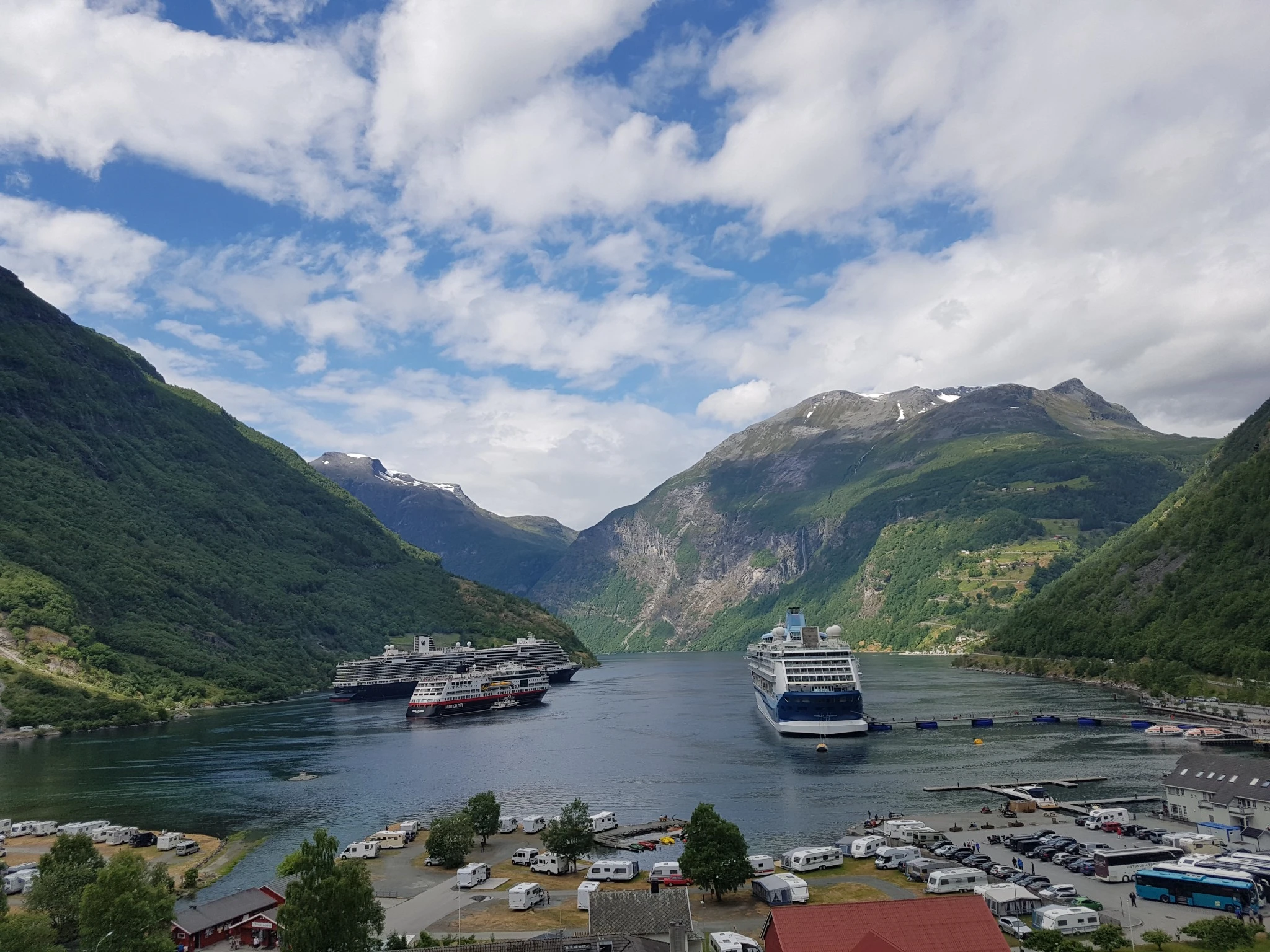 노르웨이 게이랑에르 피오르드 전경, 양쪽으로 푸른 산과 절벽이 펼쳐지고, 세 척의 대형 크루즈선이 맑은 바다 위에 정박해 있으며, 해안가에는 캠핑카와 마을 건물이 자리한 평화로운 풍경