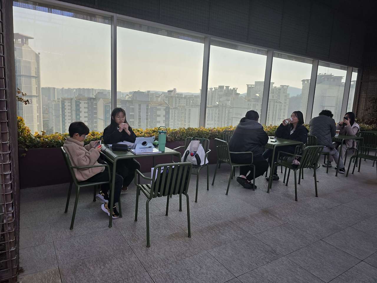 큰 창 너머 도시 풍경이 보이는 판교 현대백화점 휴식 공간에 앉아 있는 사람들
