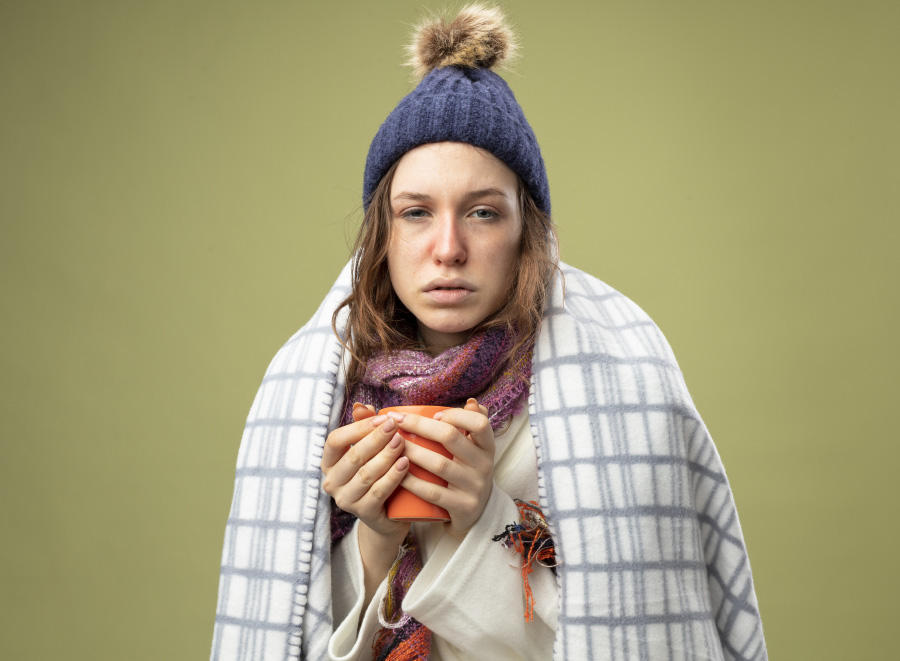 weak-young-ill-girl-wearing-white-robe-winter-hat-with-scarf-wrapped-plaid-holding-cup-tea-isolated-olive-green-900