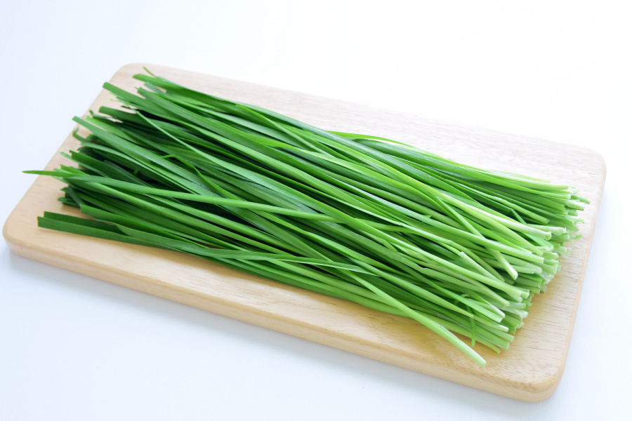 야생에서 채취를 한 부추를 하얀 바닥 위에 네모난 나무 도마를 두고 한움큼 도마 크기로 잘라서 놓아두고 찍은 사진