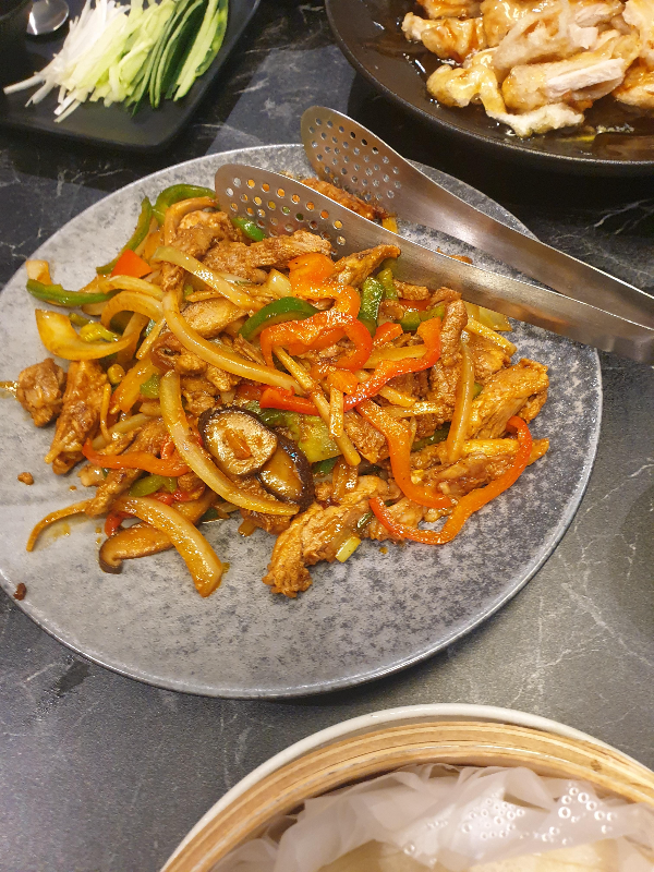 회색 접시 위에 오리 볶음이 올려져 있다. 접시에 집게도 놓여있다.