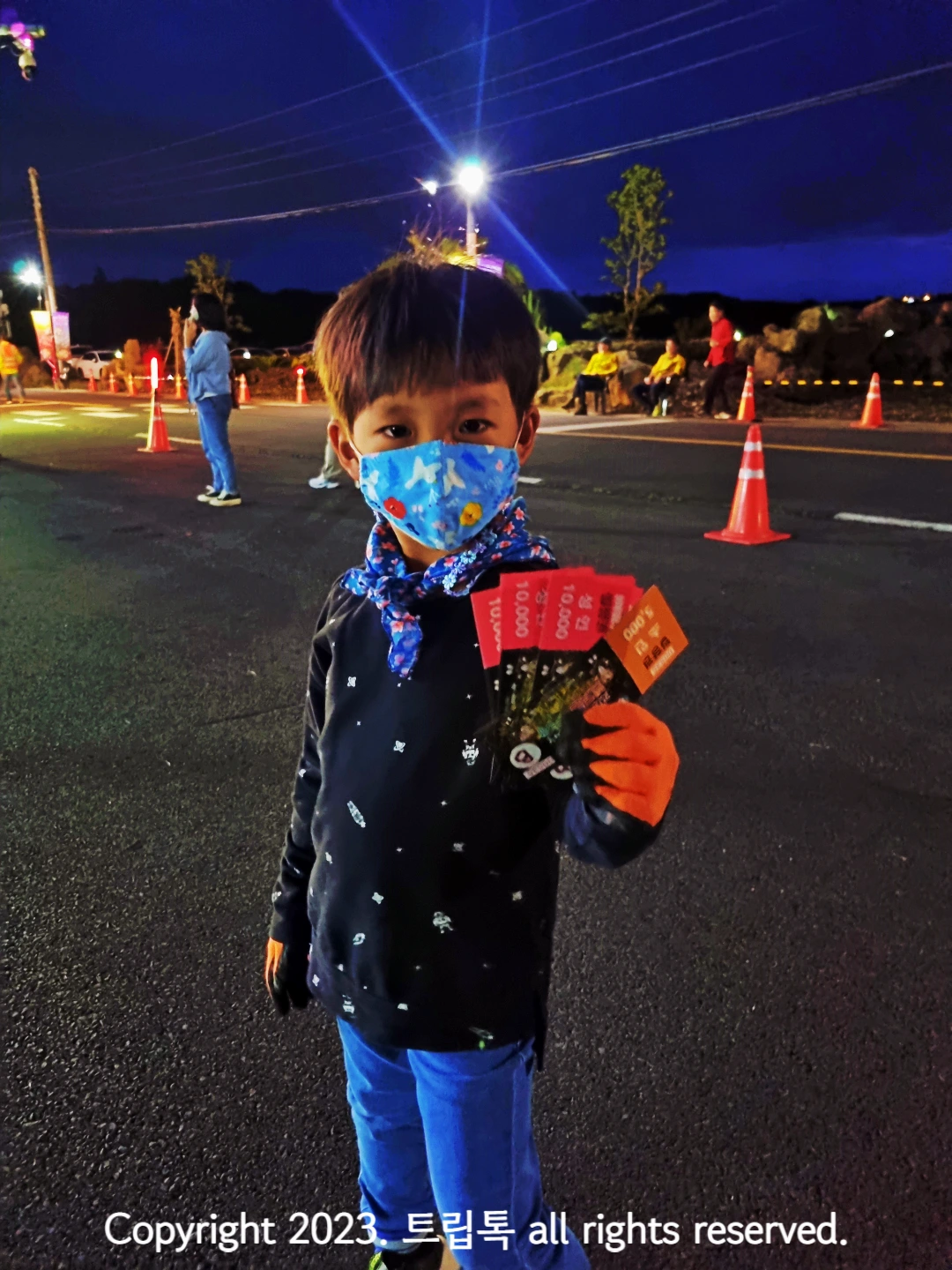 까만옷을 입고 파란 마스크를 쓴 아이가 제주 반딧불이 축제 입장권을 쥐고있다.