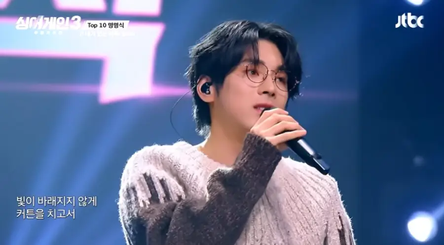 싱어게인3-
파란무대배경 웨이브진 머리 검은색 안경 분홍색 스웨터 검은 마이크를 들고 노래하는 58호