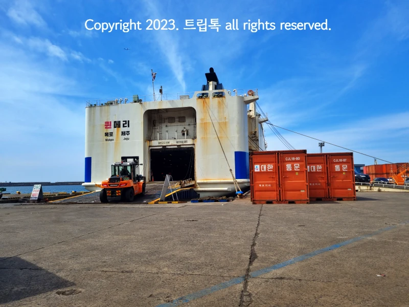 푸른 하늘과 퀸메리호의 차량이 나오는 곳의 모습니다. 왼쪽은 배가 있고 오른쪽은 대한 통운 빨간 컨테이너 박스가 있다.
