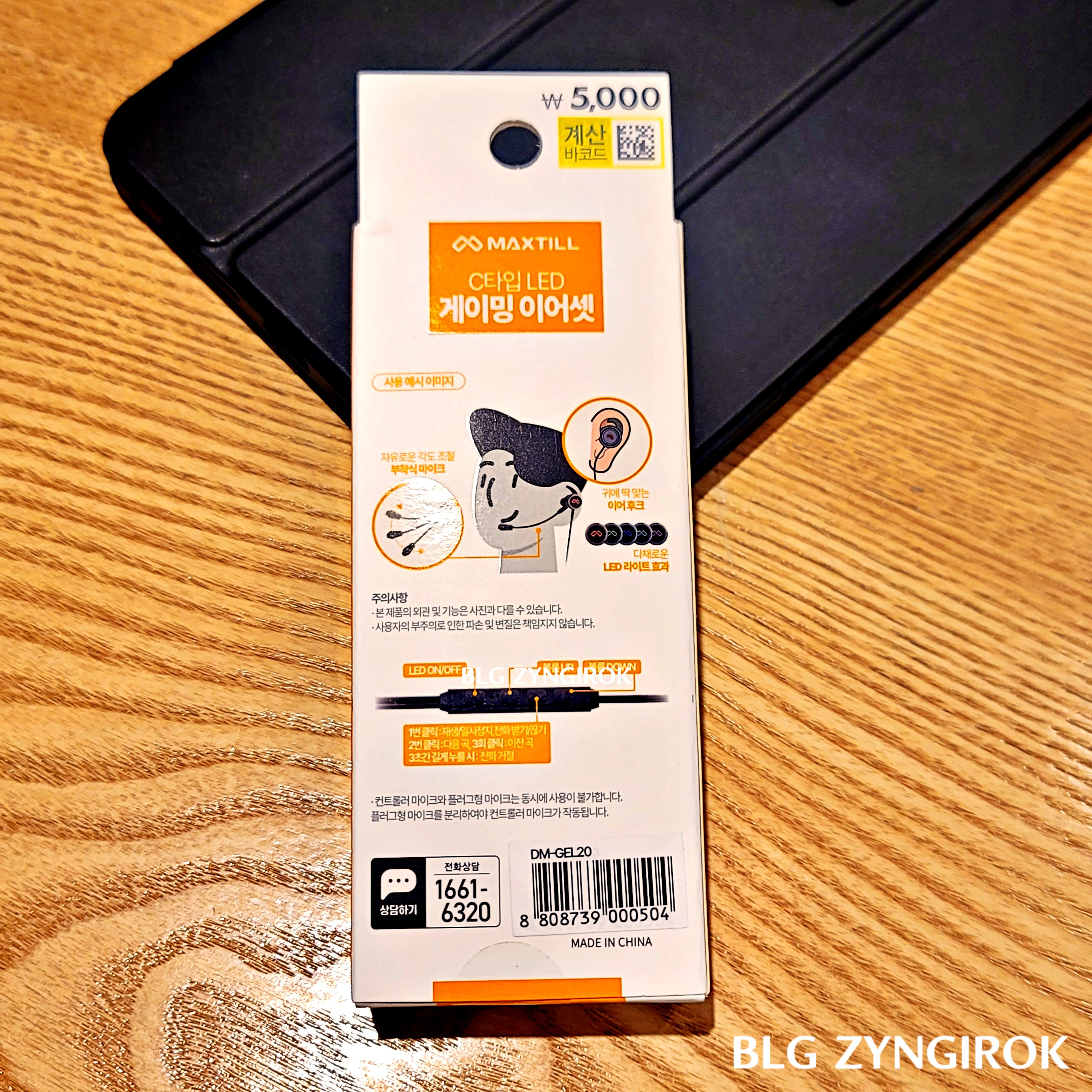 다이소 - MAXTILL 게이밍 이어폰 상자가 뒷면이 보이도록 테이블 위에 놓여있다.