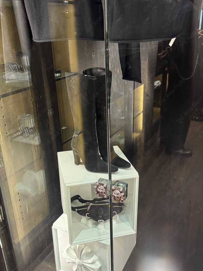 High-end Chrome Hearts black leather boots and waist bag displayed inside a glass showcase