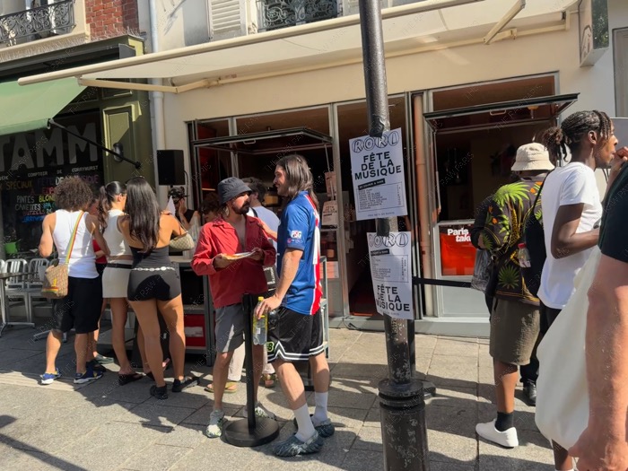 People gathering in front of a Parisian bar with Fete de la Musique event posters on the street ❘ Paris Music Festival⁠