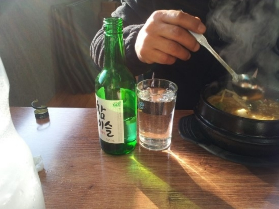 어느 식당의 한 남성이 해장국과 함께 소주병에 있는 소주를 투명한 물컵에 가득 따라 놓고 해장술을 하고 있는 것을
찍은 사진