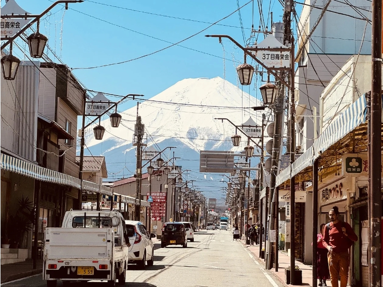 후지산이 배경으로 보이는 일본의 전통적인 상점가 거리 모습. 맑은 하늘과 설산이 어우러져 평화로운 분위기를 연출하고 있다.