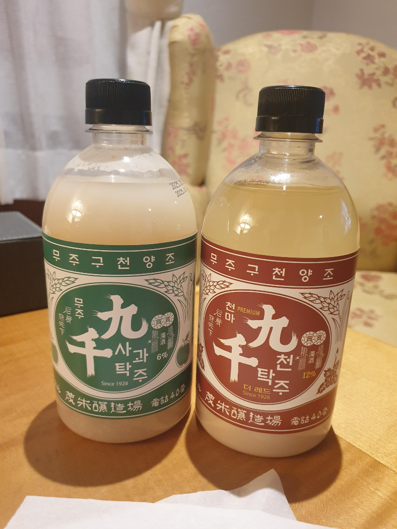 두 병으 막걸리가 테이블 위에 올려져 있다. 왼쪽은 초록, 오른쪽은 붉은 라벨
