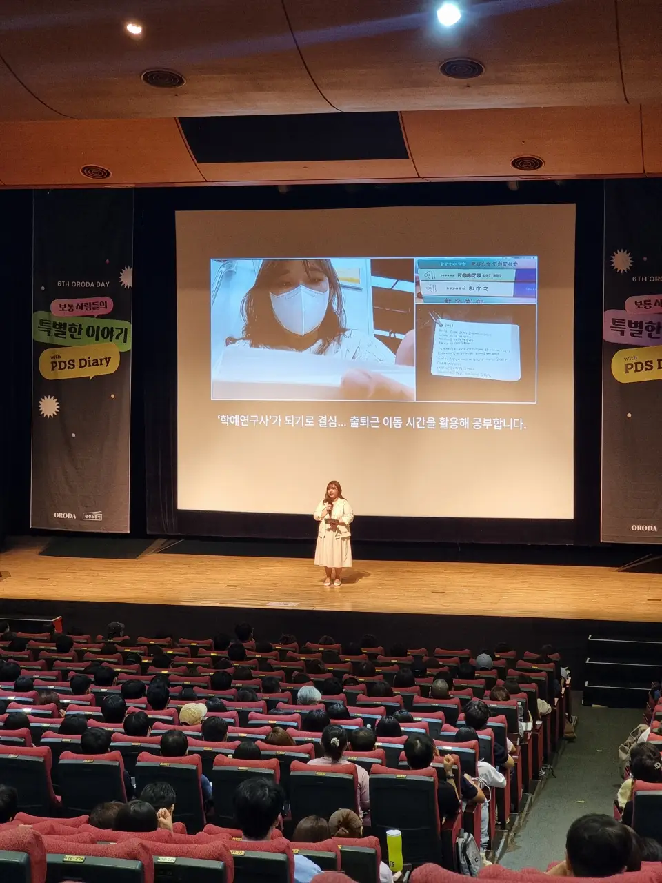 강연장-무대-마이크-들고-발표하는-여성