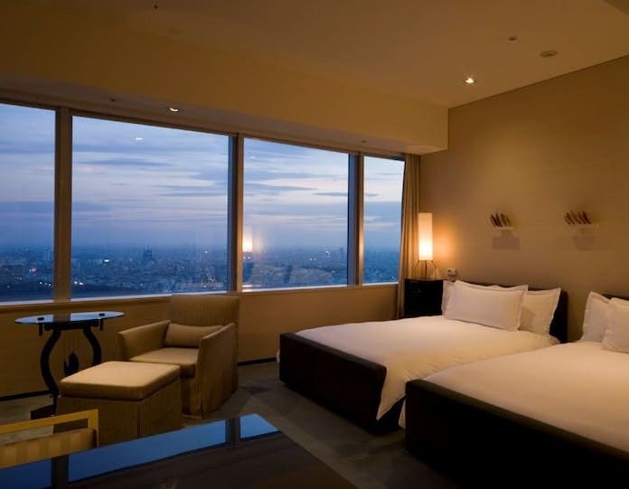 침대가 놓여져 있고 창문으로 빌딩들이 보이는 사진