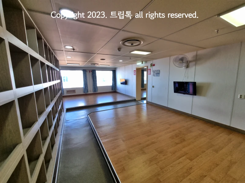 이코노미 객식의 모습으로 복도가 있고 양쪽으로 장판이 깔려있고 벽에 사물함과 창문이 보인다.