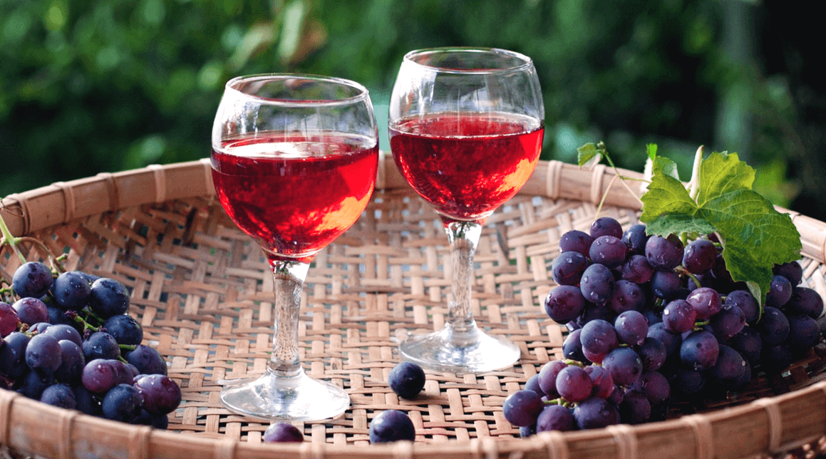 넓은 바구니에 레드와인이 담긴 유리잔 2개가 있고 검정 포도들이 담긴 장면이다.