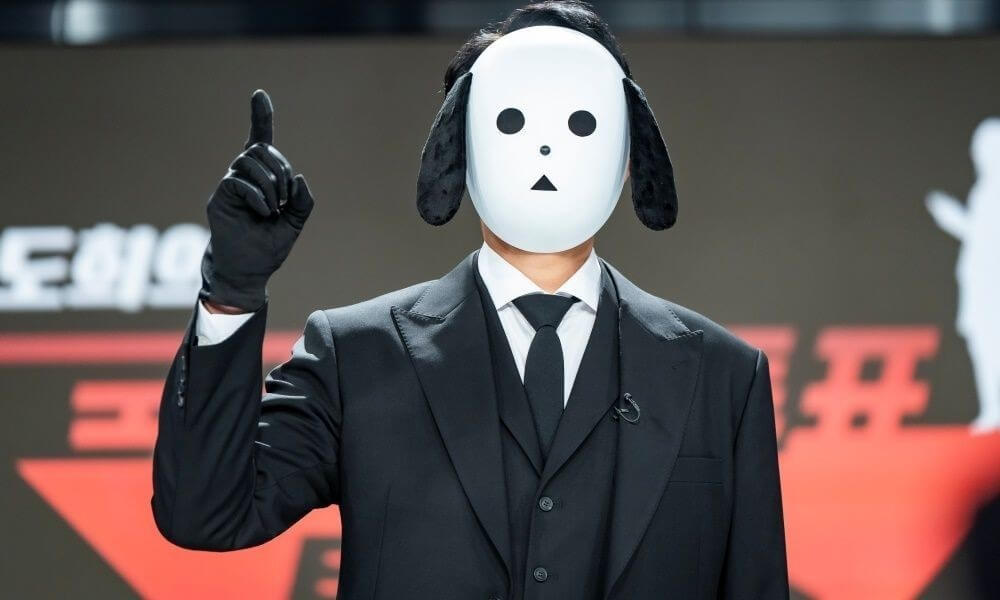 강아지 마스크를 쓴 배우가 손가락을 치켜세우고 있는 모습